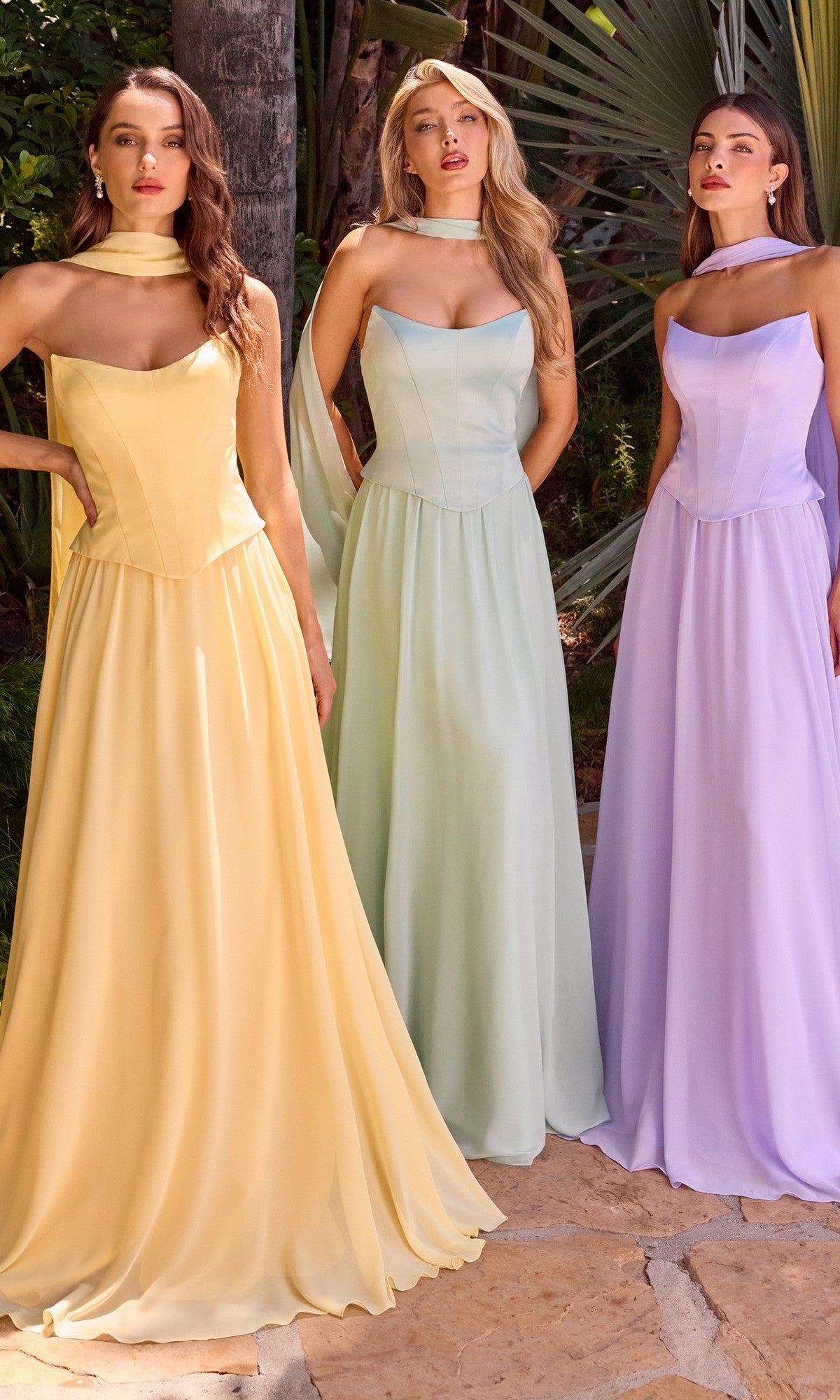Three women stand outdoors in Strapless Long Corset Prom Dresses (Ladivine CD386) in pastel yellow, mint green, and lavender chiffon with matching scarves, surrounded by greenery.